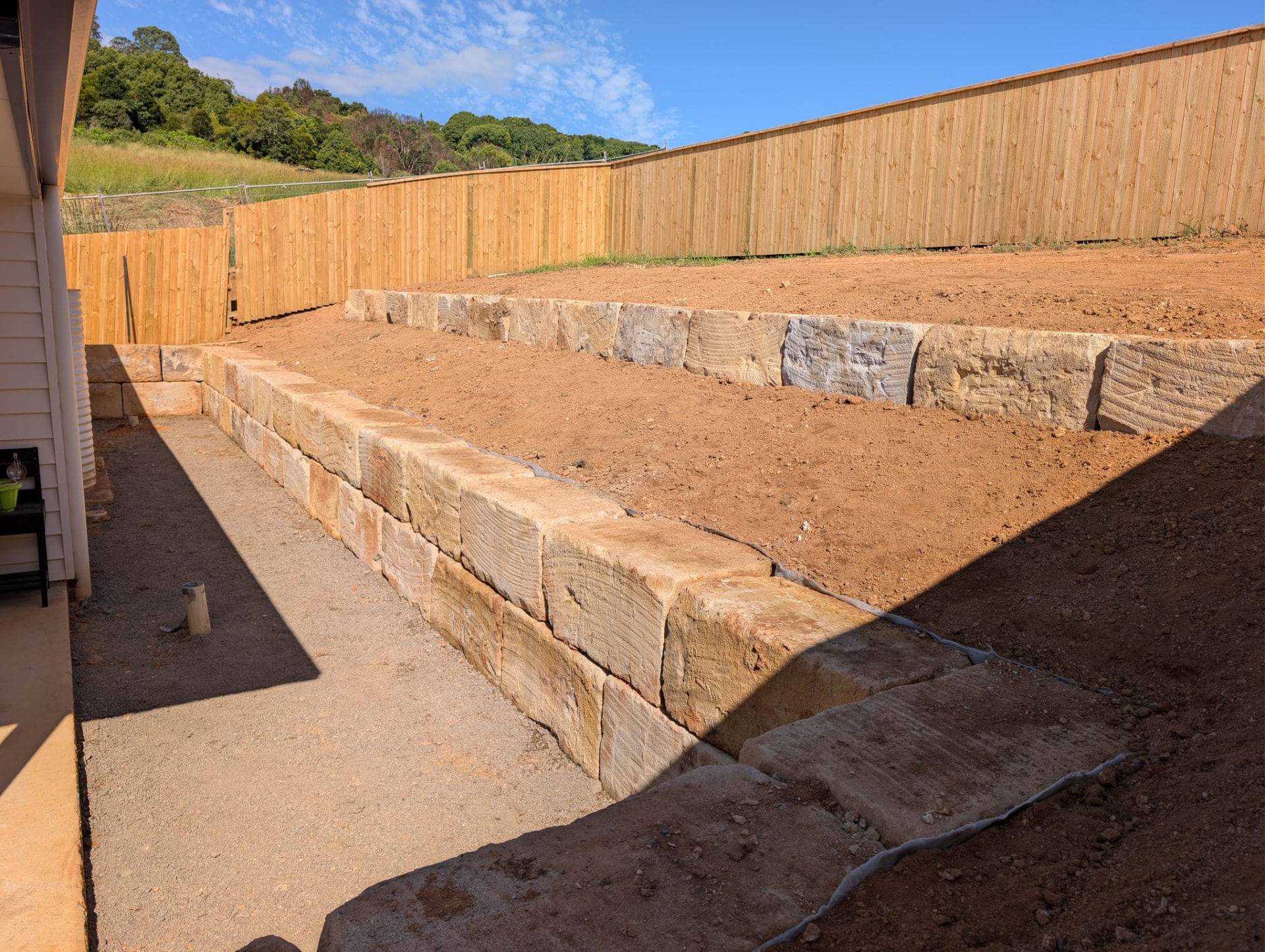 Sandstone block retaining walls terraced across a graded backyard